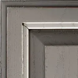 Close-up of weathered gray wooden cabinet door corner with white trim.