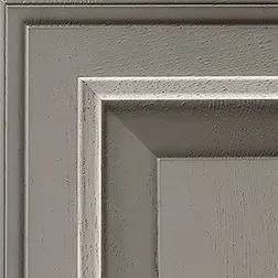 Close-up of a gray, distressed wooden cabinet door, showing raised panel and trim details.