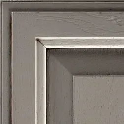 Close-up of a corner of a gray cabinet door with recessed panel and textured wood grain.