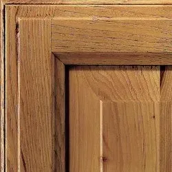 Close-up of a wood cabinet door with detailed paneling and a natural oak finish.