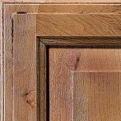 Close-up of a wooden cabinet door corner with a raised panel, showcasing wood grain and brown tones.