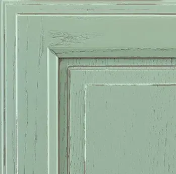 Close-up of a distressed, mint green cabinet door corner. Features visible wood grain and paint wear.