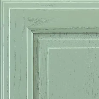 Close-up of a distressed, light green cabinet door corner, showing layered panels and visible wood grain.