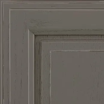 Close-up of a grey, distressed cabinet door corner, showing raised panel and trim details.