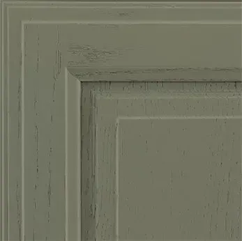 Close-up of a distressed sage green cabinet door corner with layered paneling.