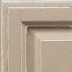 Close-up of a cabinet door corner. Light beige paint with visible wood grain and subtle white accents.