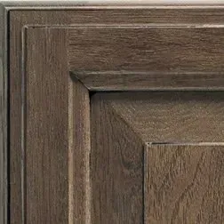 Close-up of a wooden cabinet door in shades of brown with a square, recessed panel.