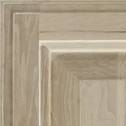 Close-up of a light-colored wood cabinet door with raised panel and beveled edges.