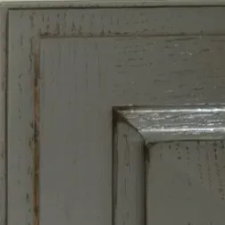 Close-up of a distressed gray cabinet door showing paint wear and wood grain texture.