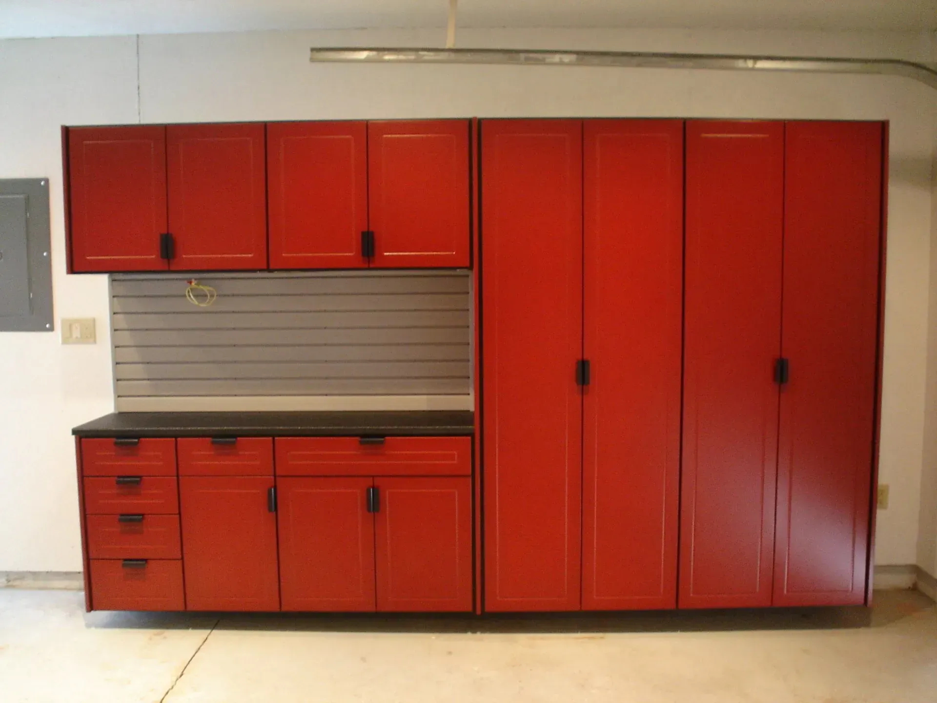 Red garage cabinets with black handles, drawers, and a grey pegboard on a concrete floor.