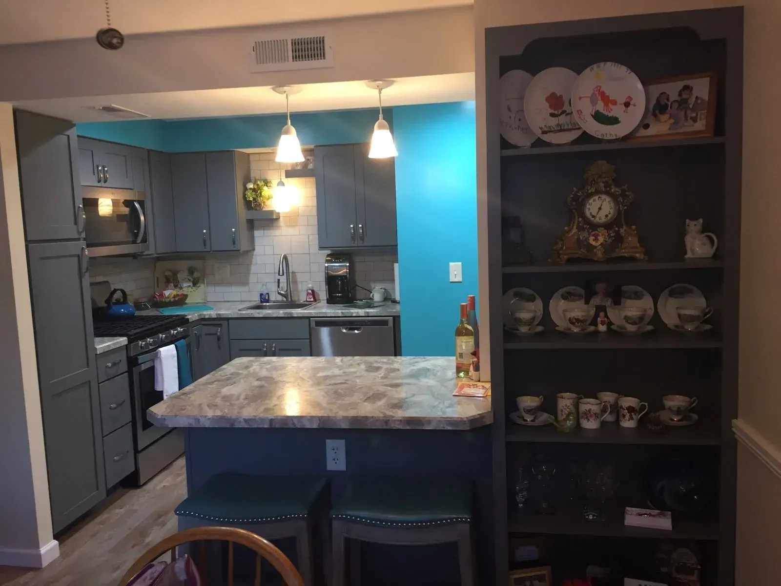 Kitchen with gray cabinets, teal wall, island with stools, and a bookshelf.