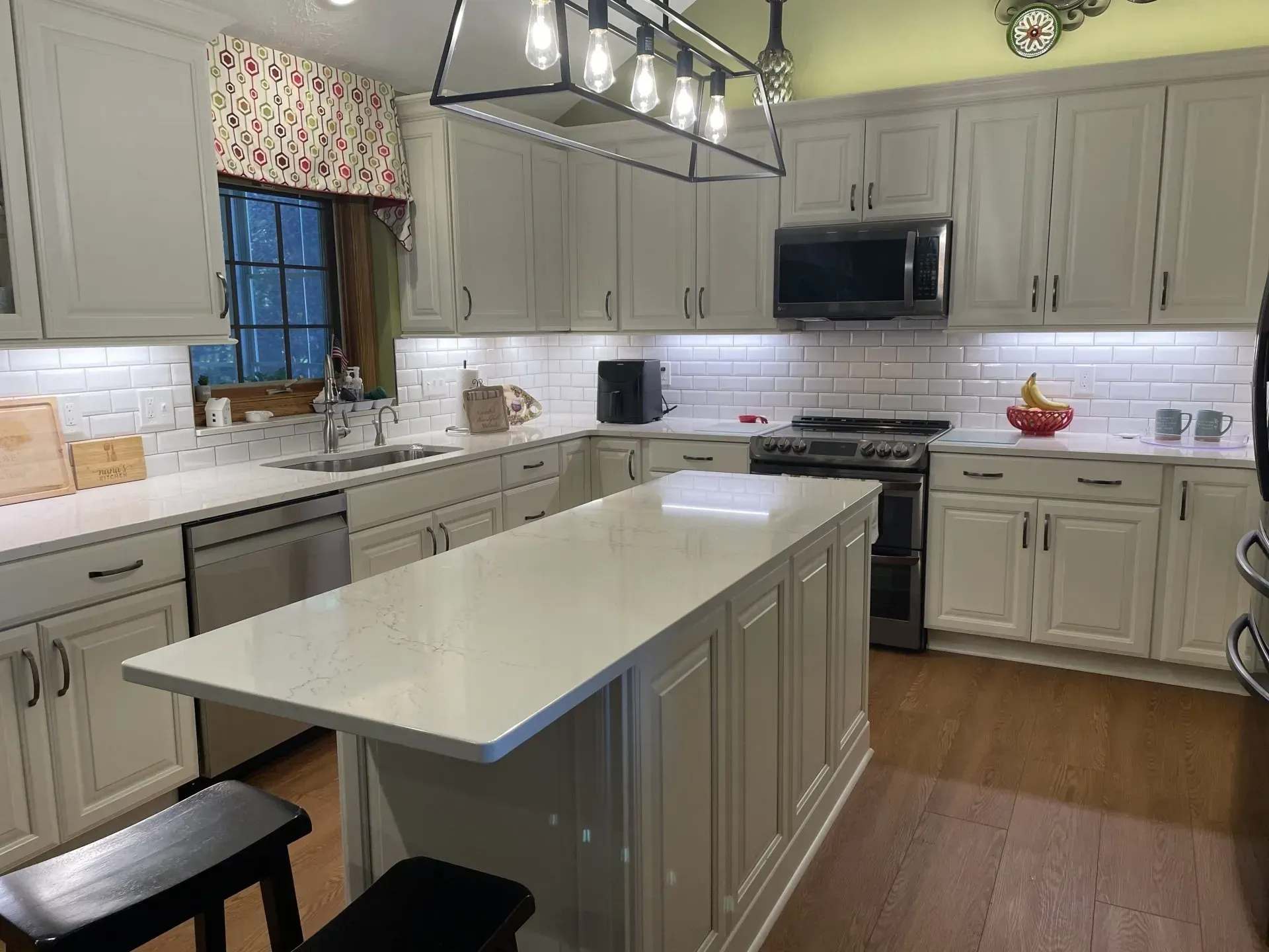 Kitchen with gray cabinets, white countertops, an island, and a dark wood floor.