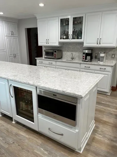White kitchen with island, granite countertops, built-in appliances, and light wood-look floors.
