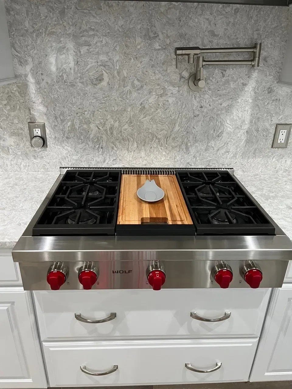 Stainless steel range with red knobs, cutting board, and granite backsplash.
