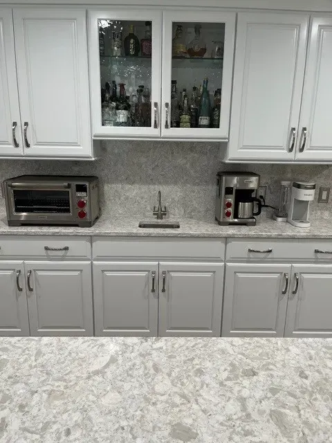 Kitchen counter with appliances, cabinets, and a wet bar with liquor bottles behind glass.
