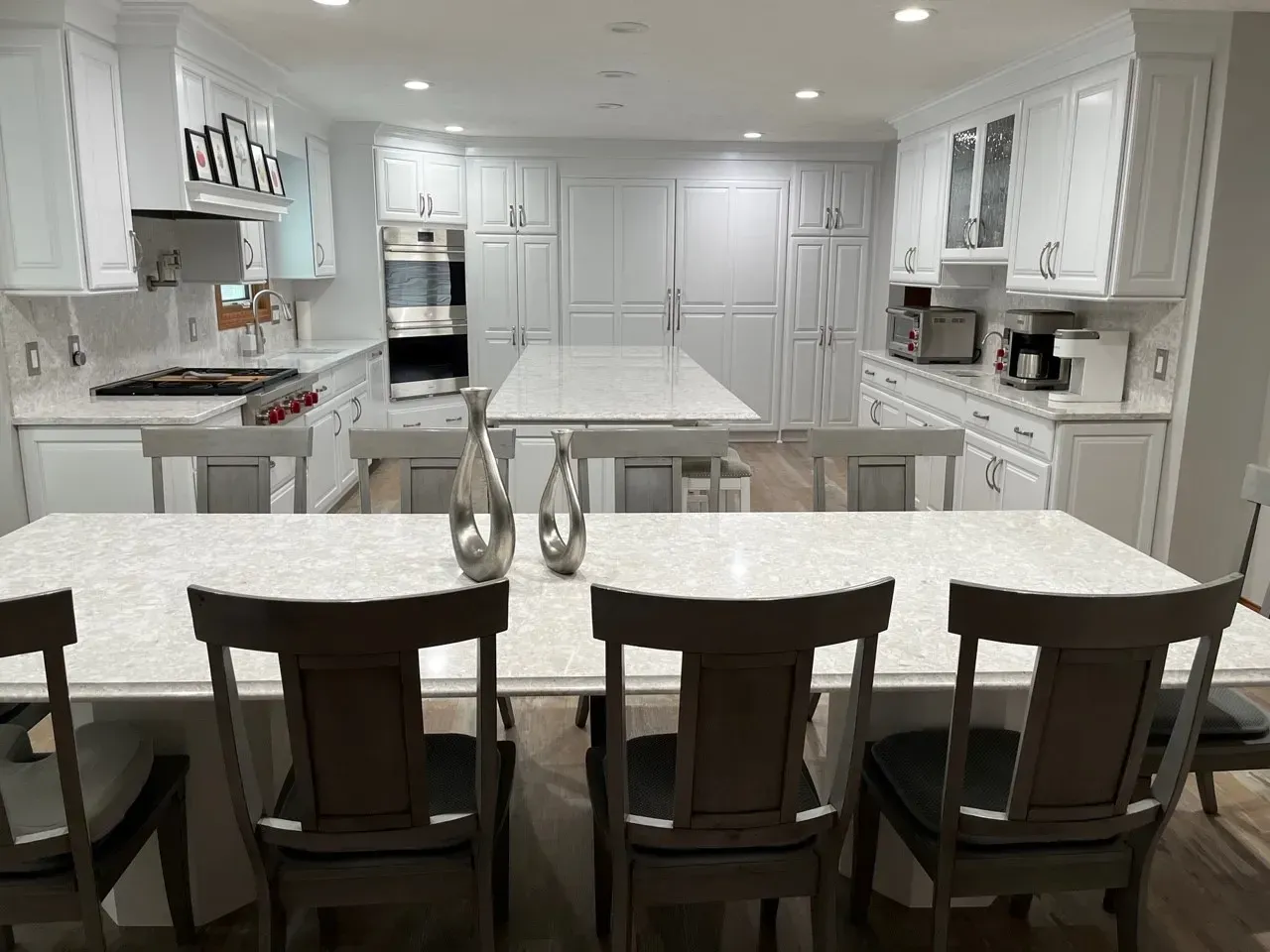 Bright white kitchen with island, table, and seating; two silver vases.