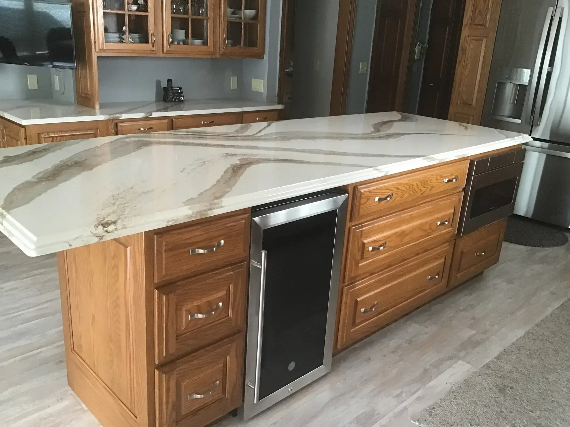 Kitchen island with a marble countertop and wooden cabinets, with a wine cooler and drawers.
