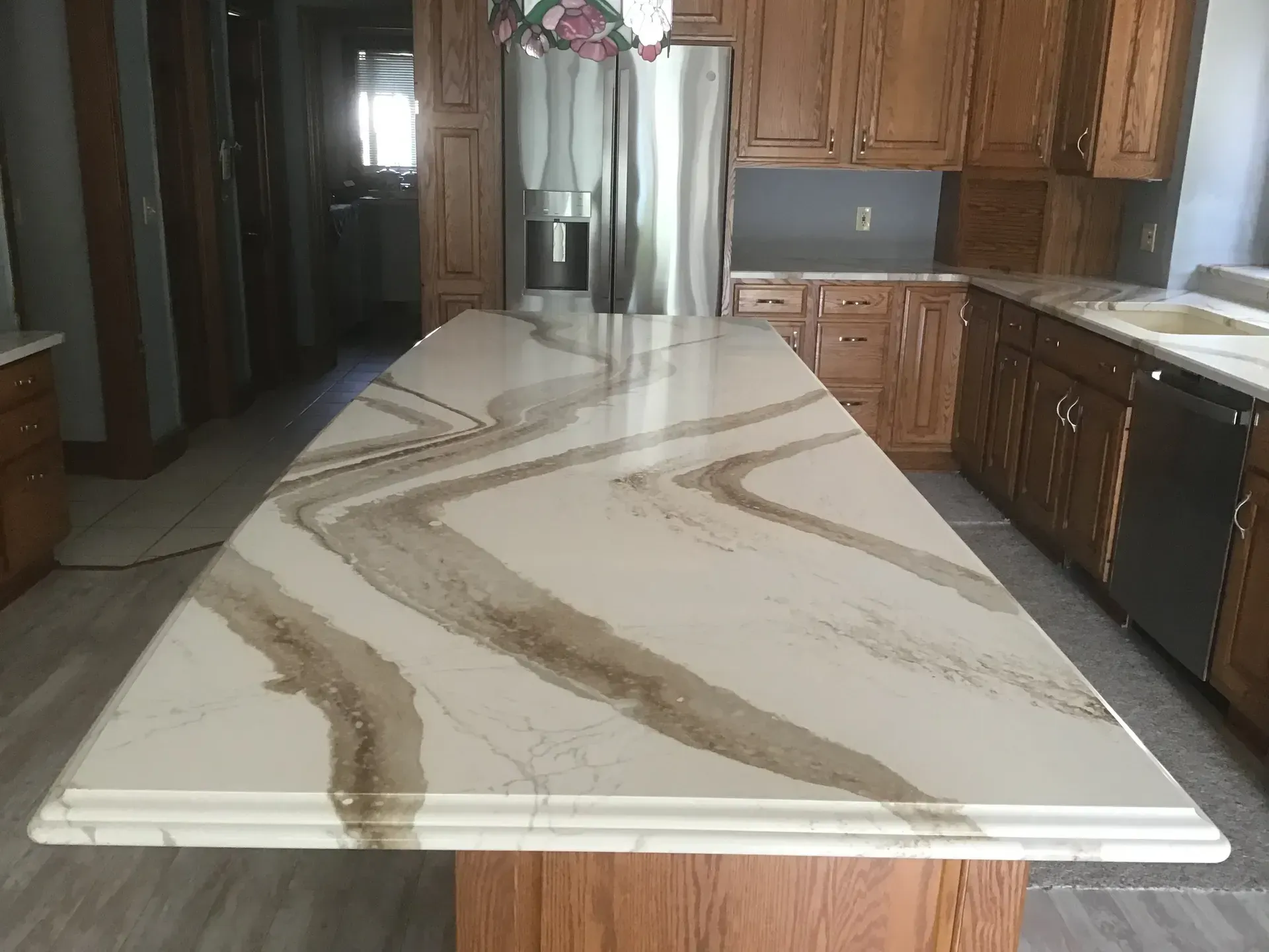 Kitchen with a large, white countertop island with brown veining. Wooden cabinets and stainless steel appliances are visible.