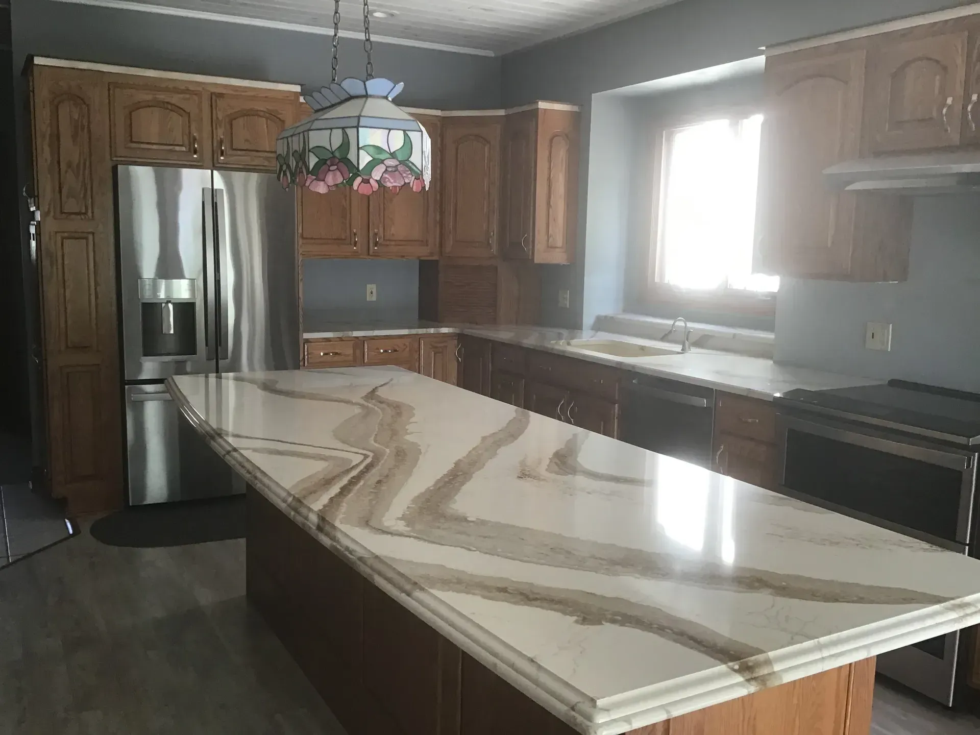 Kitchen with wood cabinets, stainless steel fridge, and a large island with a beige countertop.