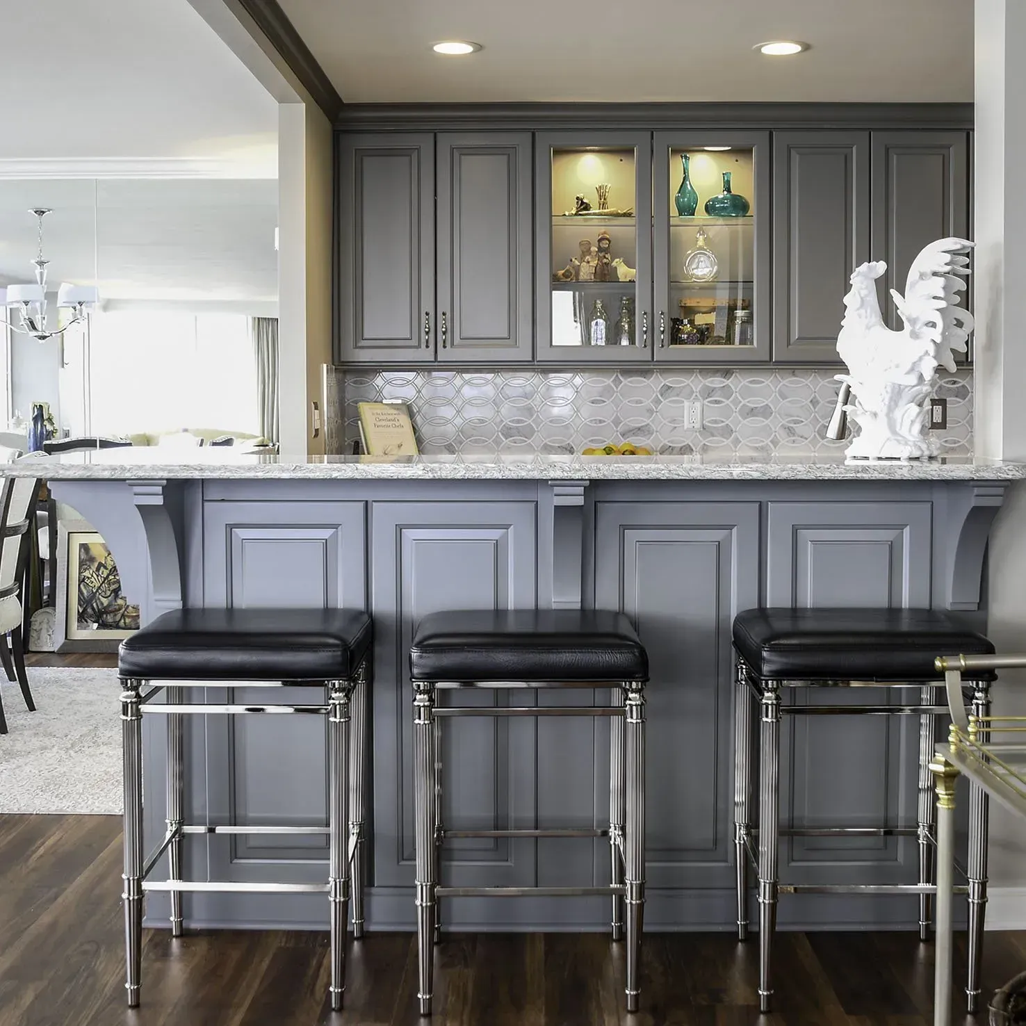 Gray kitchen bar with stools, cabinets, granite counter, and decorative white rooster.