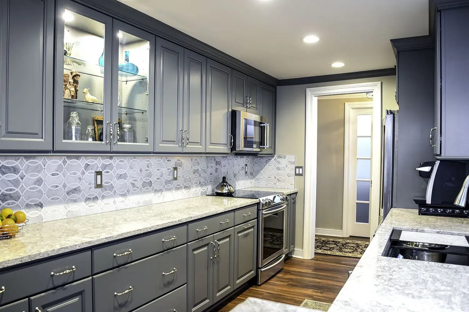 Gray kitchen with cabinets, countertops, and appliances. A door leads to another room.