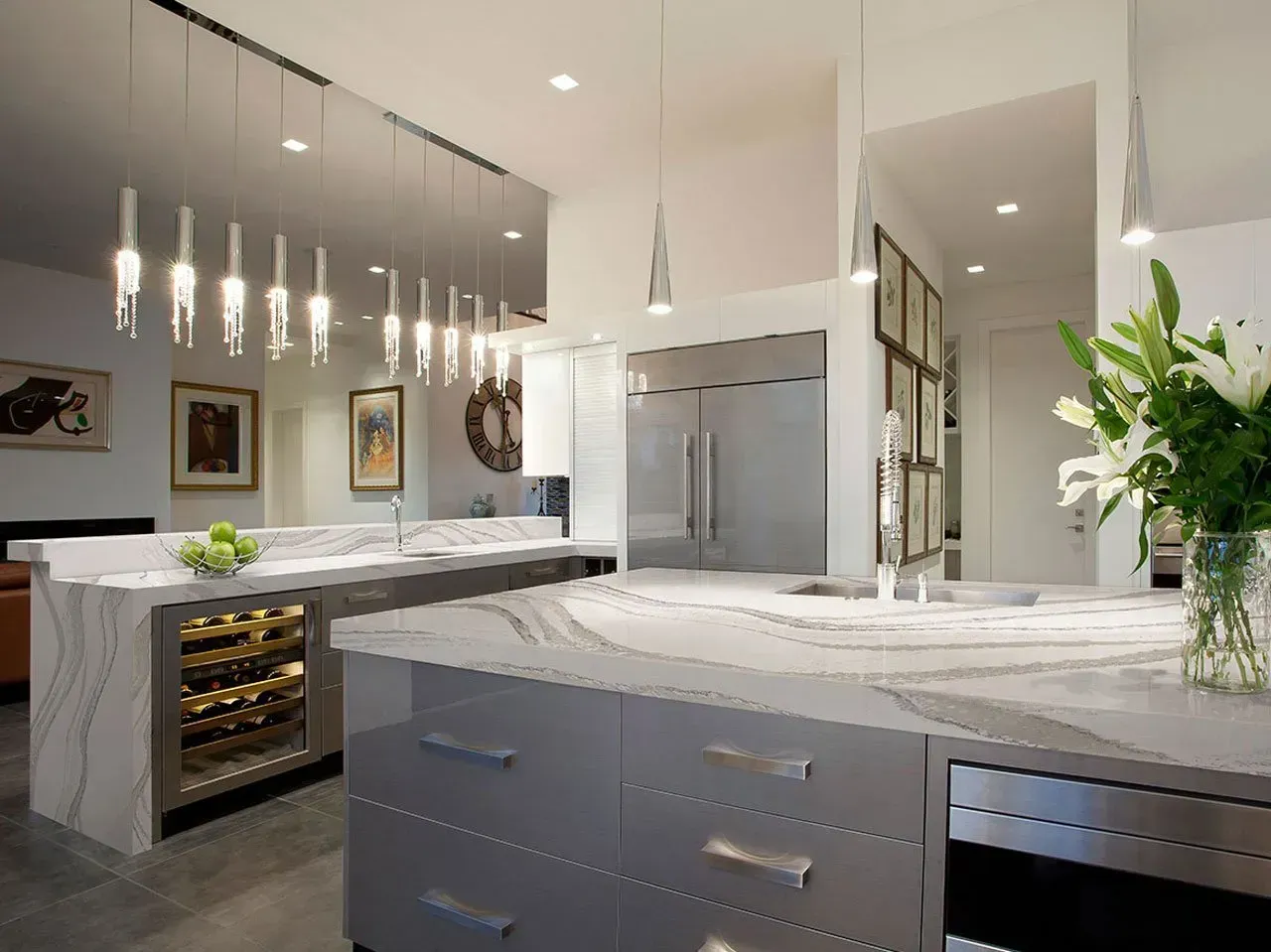 Modern kitchen with white countertops, grey cabinets, wine fridge, and decorative lights.