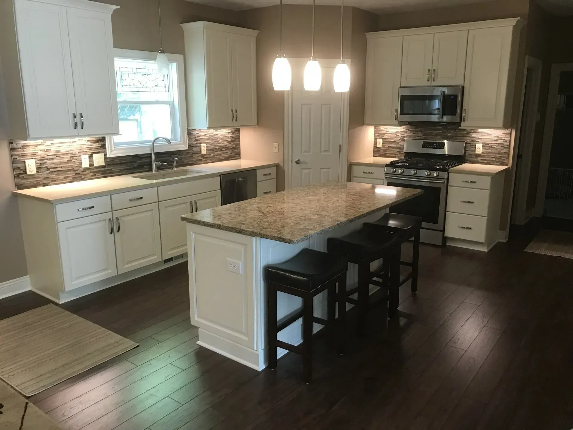 White kitchen with island, granite countertop, and dark wood flooring.
