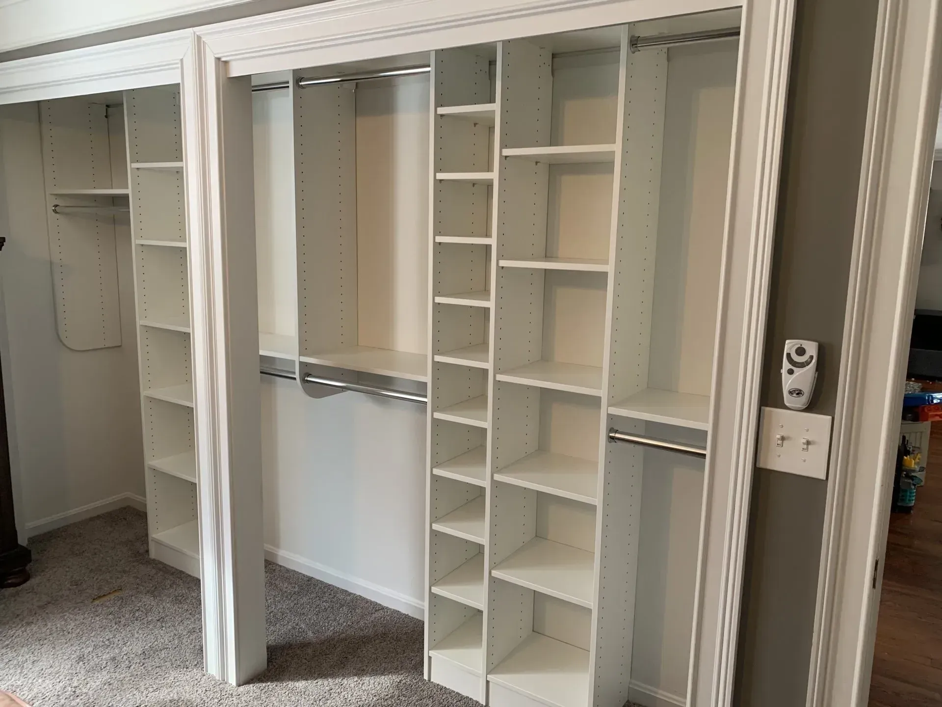 White closet with shelves, hanging rods, and built-in shelving. Gray wall and carpet are visible.
