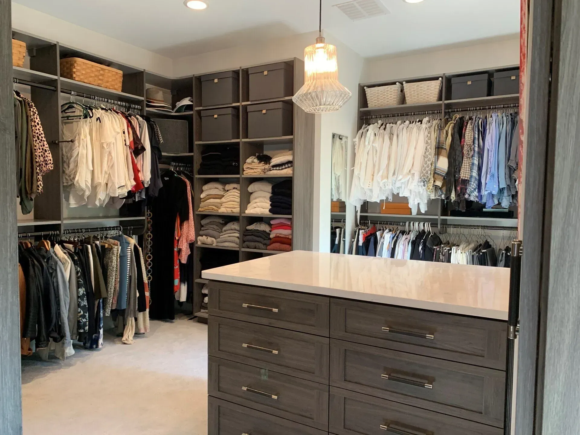 Walk-in closet with gray shelves, hanging clothes, and a central island with drawers.