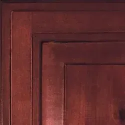 Close-up of a reddish-brown wooden cabinet door with a layered, recessed panel design.