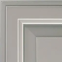 Corner of a gray cabinet door with recessed panel and layered molding.