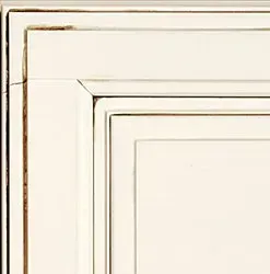 Corner of a cream-colored, distressed cabinet door showing recessed panel and decorative trim with visible wood grain.