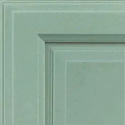 Close-up of a light green cabinet door corner with a raised panel and detailed molding.