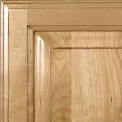 Close-up of a light brown, wooden cabinet door. Details include recessed paneling and layered frame.