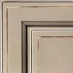 Close-up of a distressed, beige-painted cabinet door corner, showcasing its layered construction with aged details.