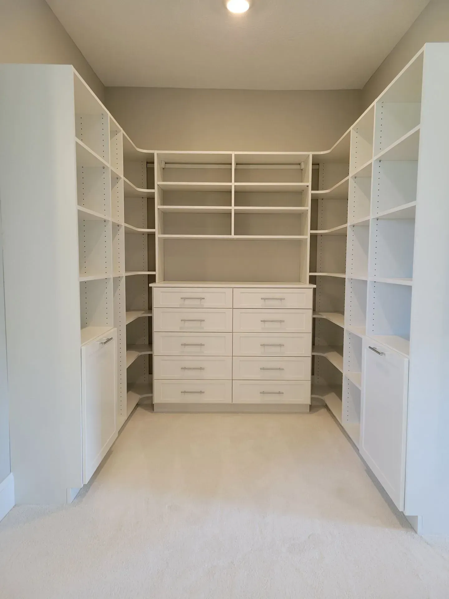 White walk-in closet with built-in shelves, drawers, and a central chest of drawers against a light gray wall.