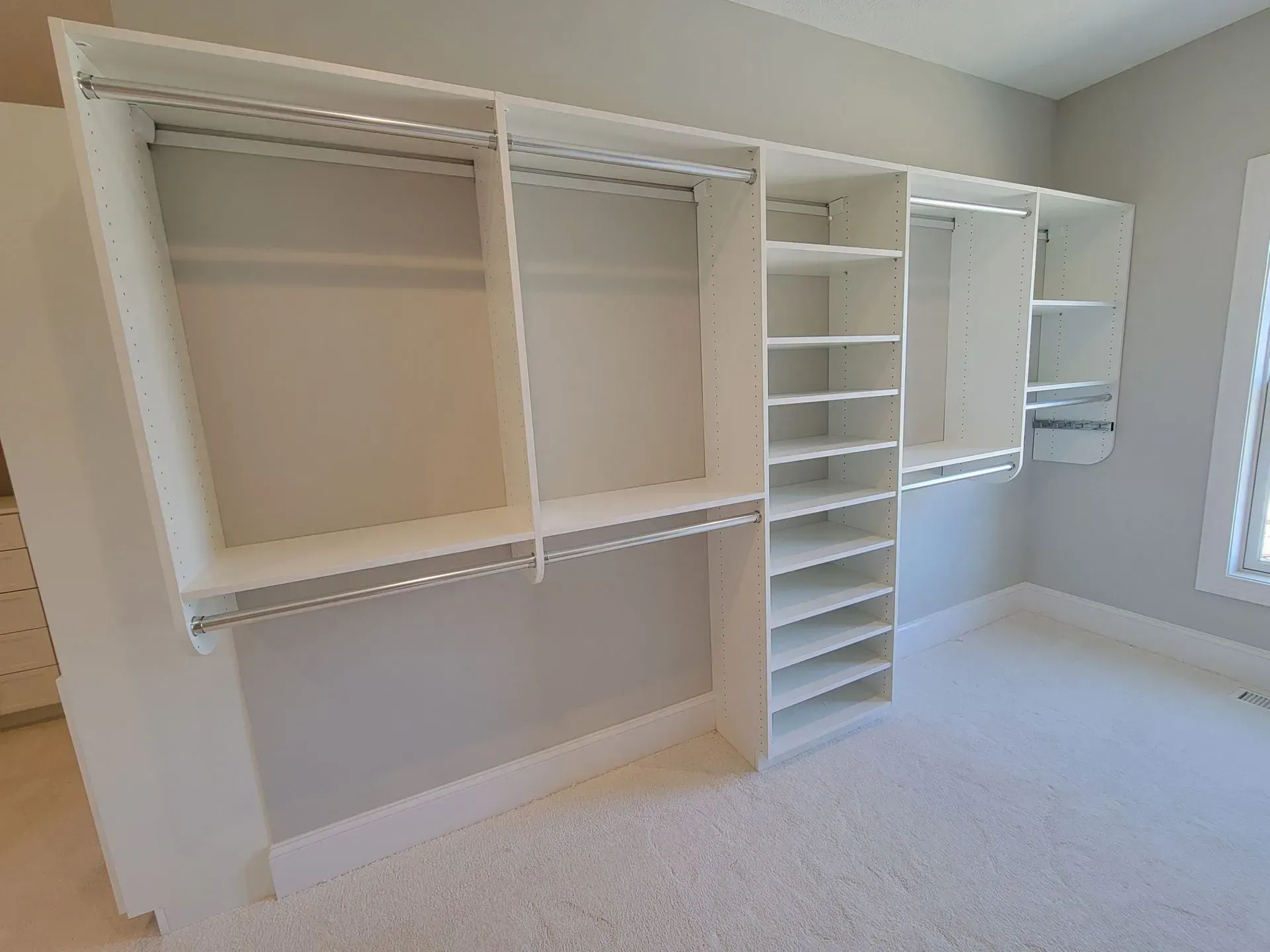 White built-in closet with shelves, rods, and a central tower. Light-colored room with carpet and a window.