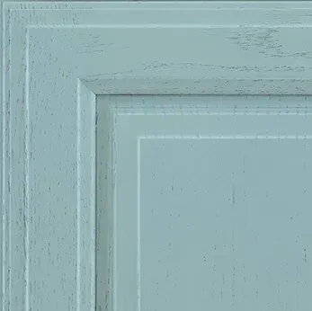 Blue-painted wood cabinet door corner with layered, raised panels and a light, distressed finish.