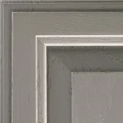Close-up of a grey, recessed-panel cabinet door with visible wood grain and trim.