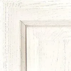 Close-up of a white-washed wood cabinet door showing wood grain texture and beveled edges.