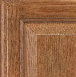 Close-up of a stained, wooden cabinet door panel, showing wood grain and detailed edges.