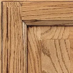 Close-up of a corner of a stained oak cabinet door with a raised panel and wood grain.