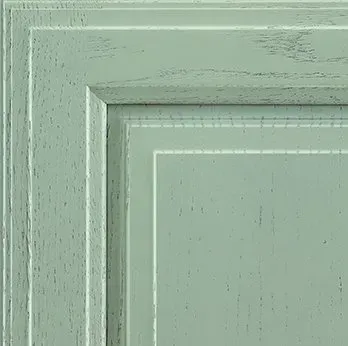 Close-up of a painted kitchen cabinet door with a light green, distressed finish.