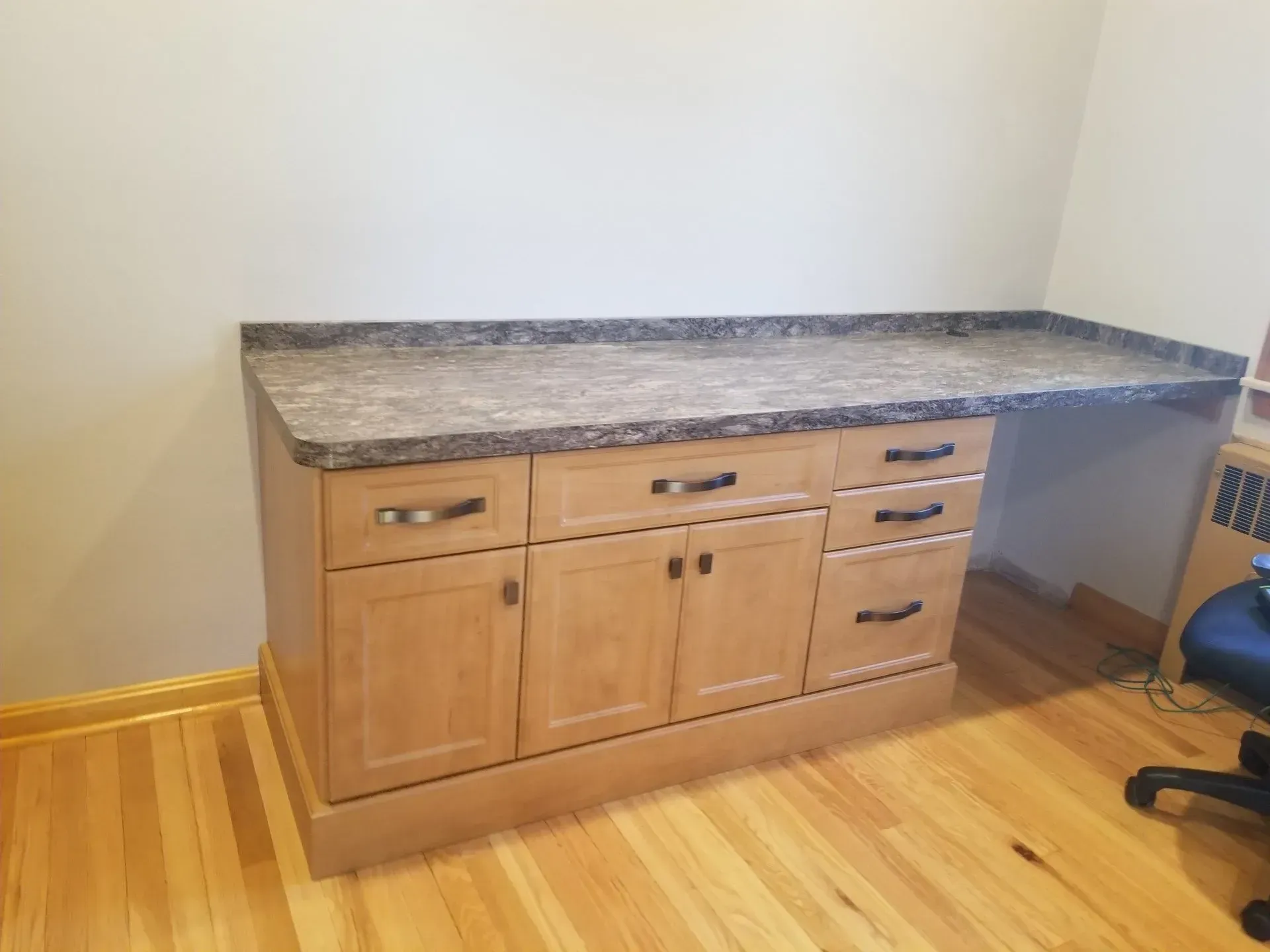Desk with light wood cabinets, drawers, and brown granite countertop against a beige wall.