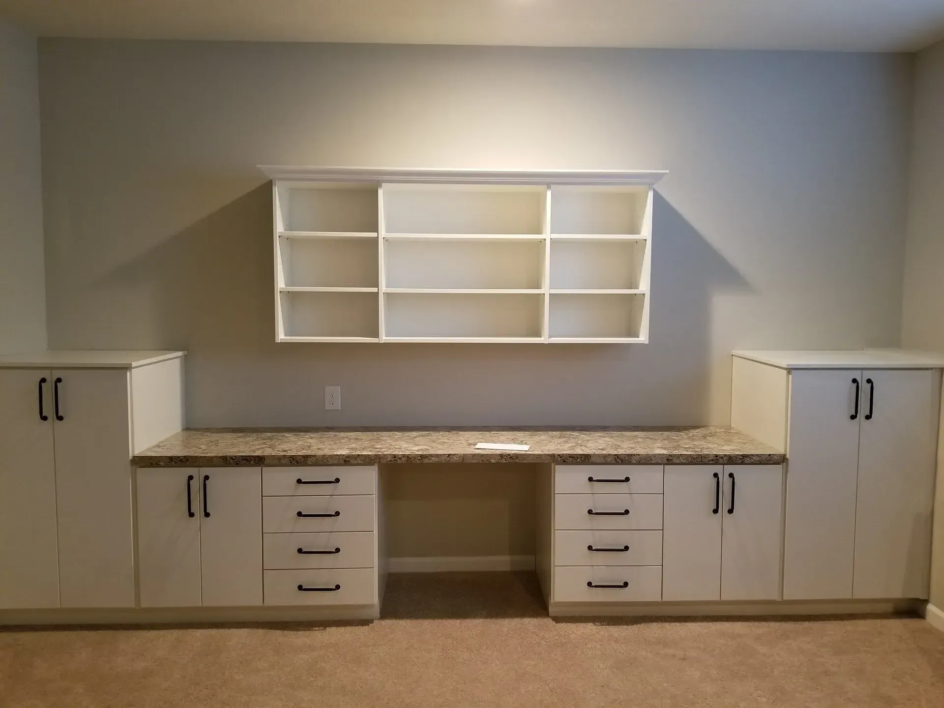 Built-in white desk and storage with drawers, cabinets, and shelving on a beige carpet.
