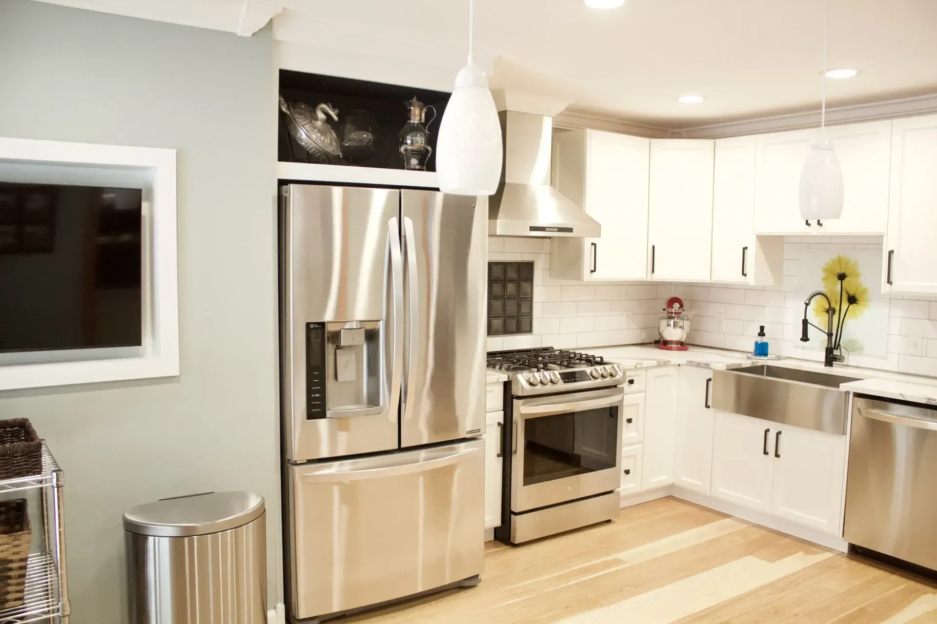 Modern kitchen with stainless steel appliances, white cabinets, and light wood floors.