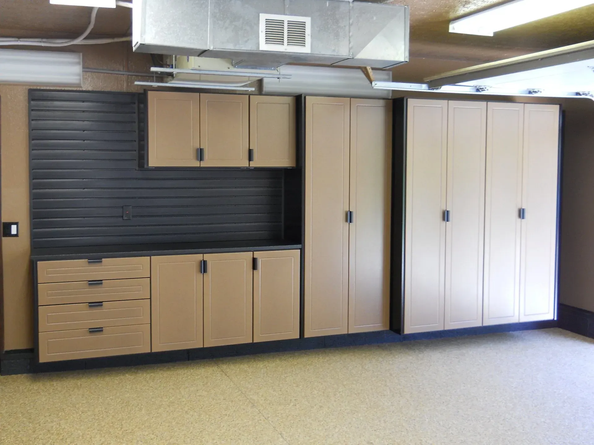 Garage storage cabinets in tan and brown with a black slat wall.