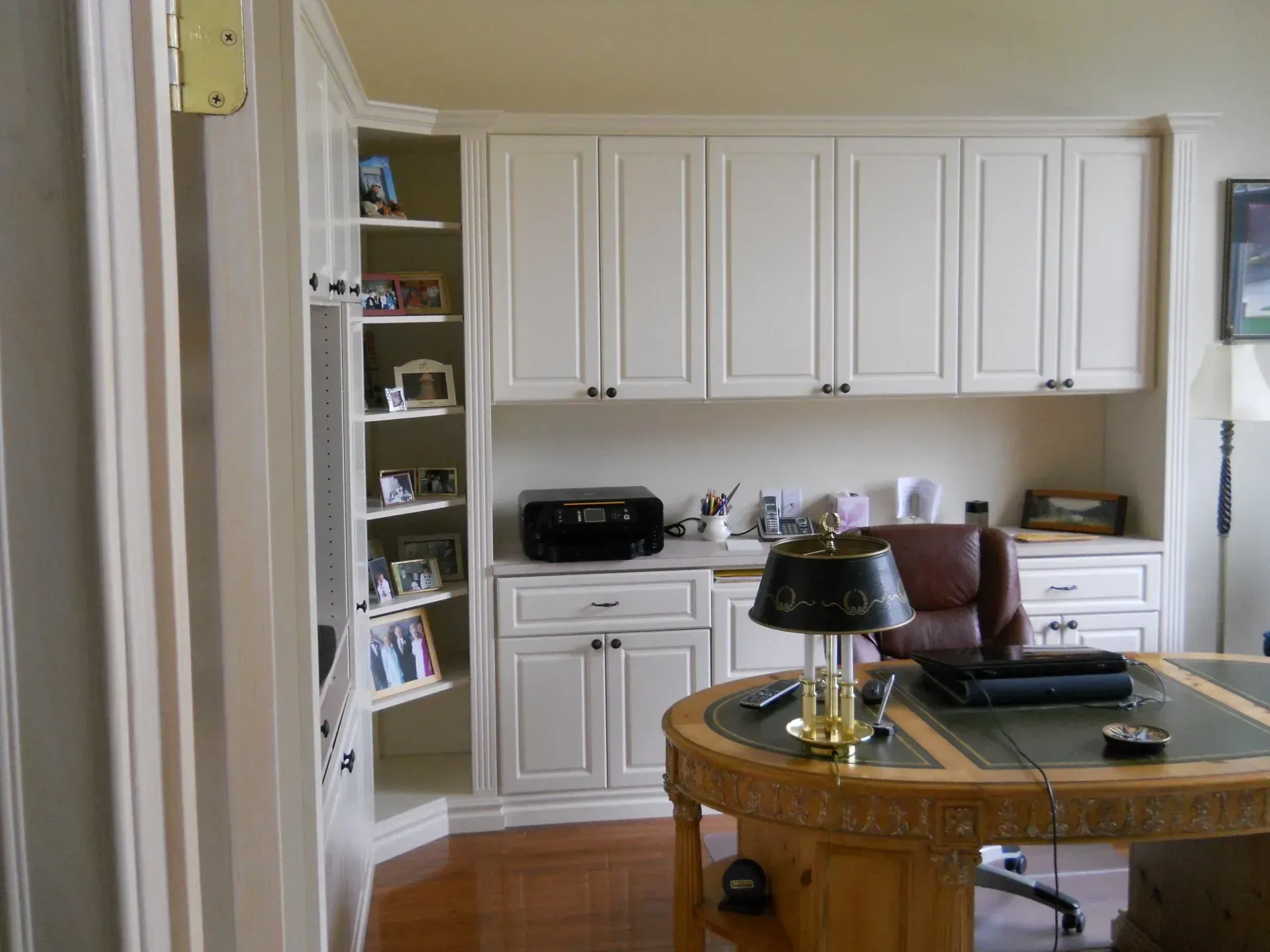 Cream-colored office with desk, chair, built-in cabinetry, and a side shelving unit.