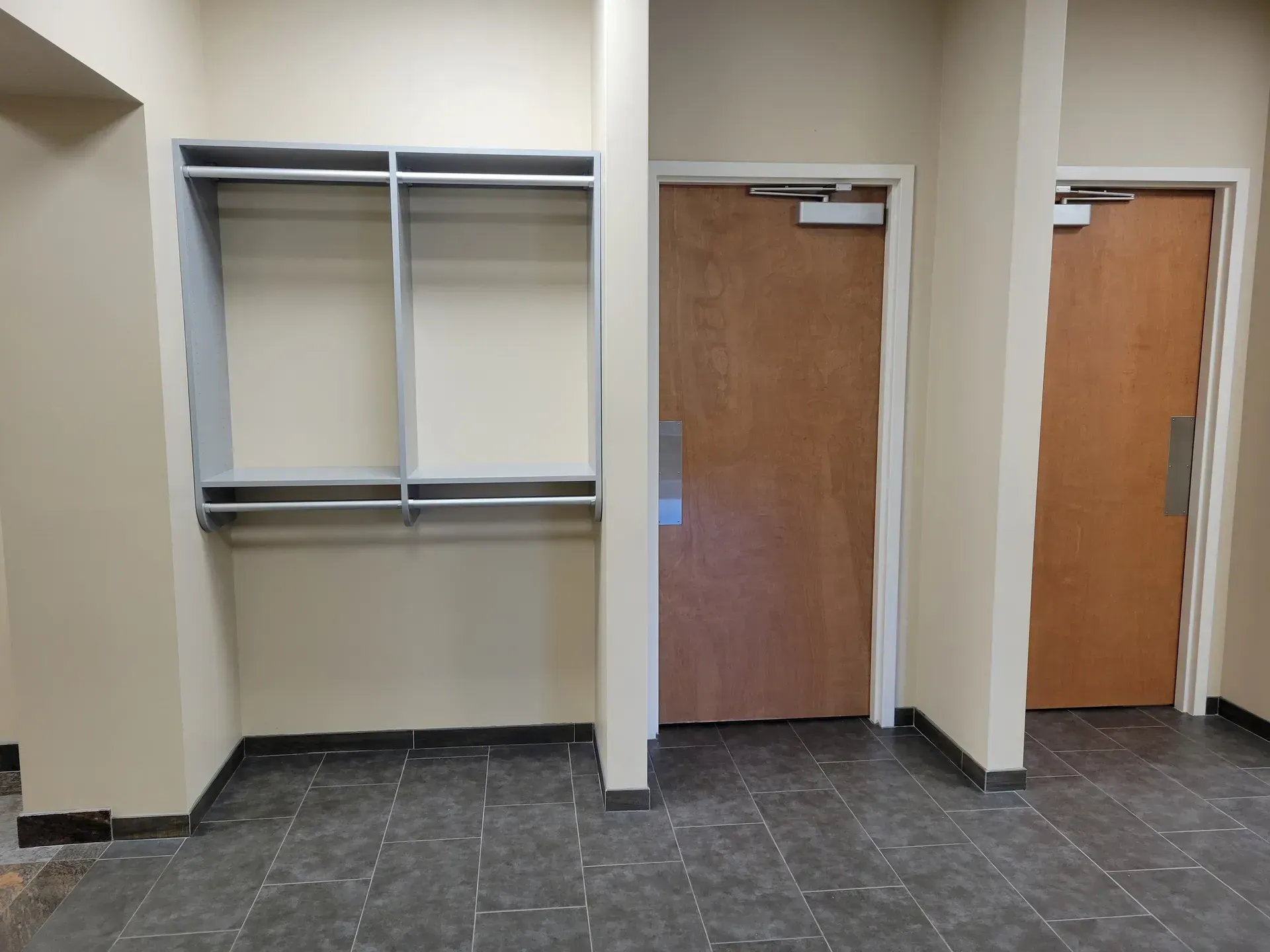Hallway with closet and two brown doors. Black tile floor, beige walls, gray closet frame.
