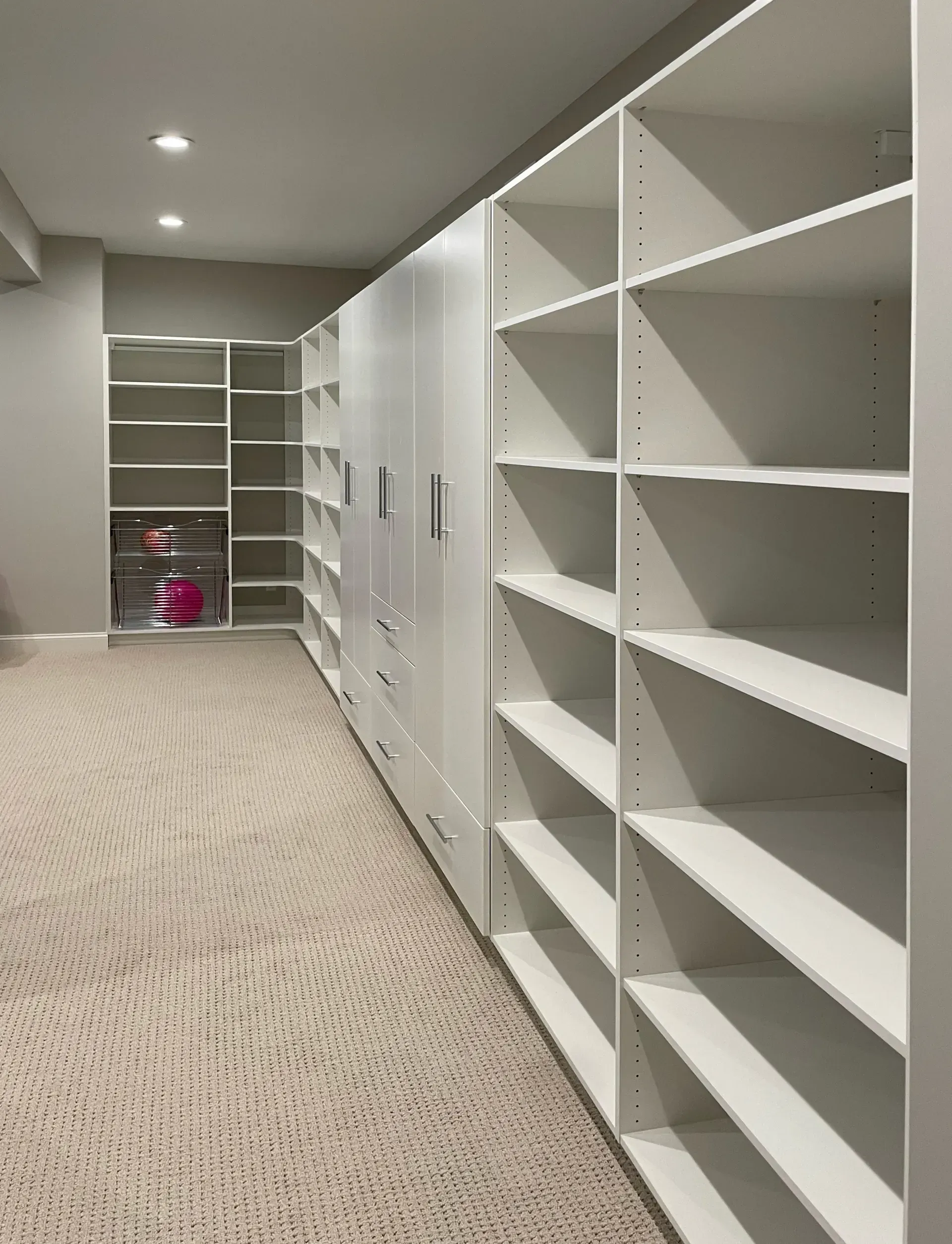 Built-in white shelving and cabinets line the wall of a room with beige carpet.